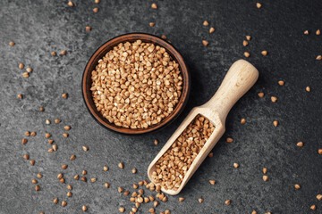 Buckwheat grains in a bowl with a wooden scoop on a dark stone background
