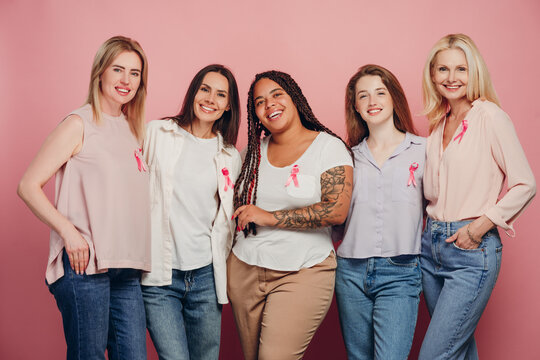 Women of different ethnicities wearing pink ribbons are embracing for breast cancer awareness