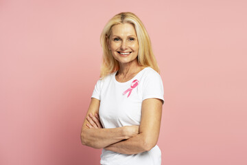 Smiling woman wearing pink ribbon is posing with crossed arms for breast cancer awareness