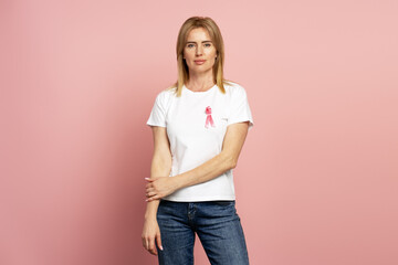 Woman wearing pink ribbon supporting breast cancer awareness posing on pink background