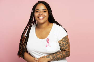 Young woman wearing pink ribbon for breast cancer awareness smiling on pink background