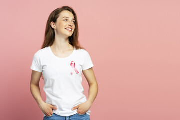 Young woman wearing pink ribbon smiling and looking away on pink background