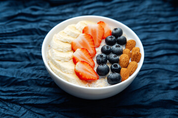 Oatmeal bowl with fruits and almonds on dark blue textile background