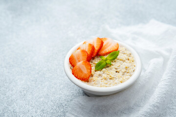 Strawberry oatmeal porridge with mint garnish in white bowl on gray surface