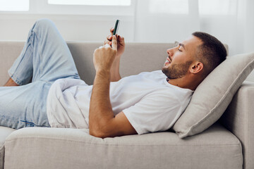 A relaxed man enjoying a digital detox while lounging on a couch, scrolling through his phone, symbolizing the balance between technology and mental well-being.