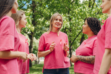 Women wearing pink ribbons supporting breast cancer awareness talking in a park