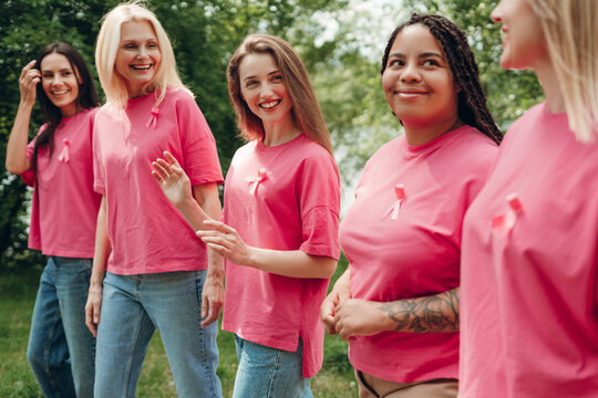 Women wearing pink ribbons supporting breast cancer awareness walking together in park - Powered by Adobe