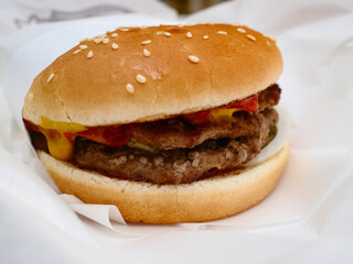 A double meat burger with ketchup and mustard on it, sitting in paper takeout container