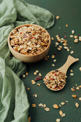 Wooden bowl and scoop of granola on green textile background