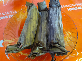 Three packets of lontong nasi wrapped in yellowish green banana leaves and tied with a stick,...