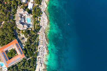the clear turquoise waters of the Adriatic Sea, rocky coastline, and a vibrant beach promenade...