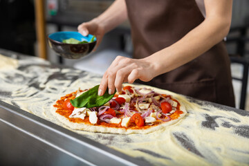 Cooker in apron working in the pizzeria kitchen and putting topping on the pizza