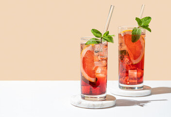 Two glasses of cocktail with grapefruit, mint and ice on marble stand on a white yellow background