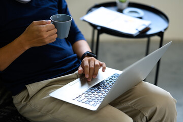 Cropped shot of man using laptop and sipping hot drink during remote work at home