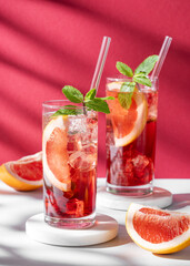 Two glasses of cocktail with grapefruit, mint and ice on marble stand on a red white background