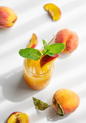 Peach drink or tea with ice, mint in a glass on a white table with fresh fruits and sunlight.