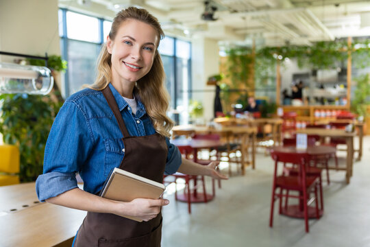 Pretty blonde woman in apron looking happy at her working place in pizzeria - Powered by Adobe