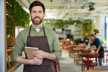 Young bearded man in apron looking confident while waiting for the client in pizzeria