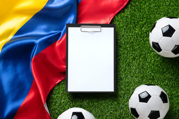 A soccer balls and clipboard with white paper sheet on a green field with a Colombian flag. High quality photo