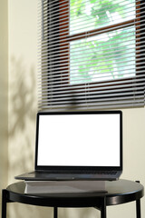 Laptop with blank screen on top of books on a black round table near window blinds