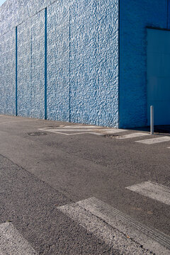 Minimalist urban scene with crosswalk and empty street beside blue wall, designed for use as copy space in technology, smart mobility and digital design themes.