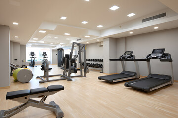 Obraz premium Modern gym with exercise equipment and wood floor.Bright and spacious modern gym interior with wooden floor, cardio machines, and weight training equipment. Health and wellness concept.