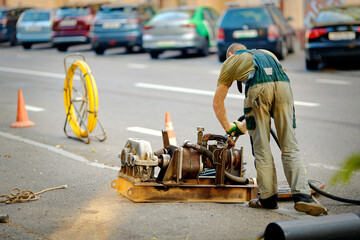 Utility worker using cable pulling rod tool to guide fiber optic cables through an open manhole...
