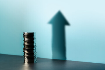 Coins stacked cast a tall upward arrow shadow, reflecting financial growth, investment optimism, and a hopeful economic outlook