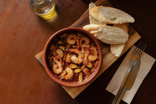 Spanish Gambas al Ajillo with Garlic and Olive Oil, Served with Baguette and Cutlery on Wooden Table