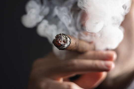 A man smokes a cigar on dark background