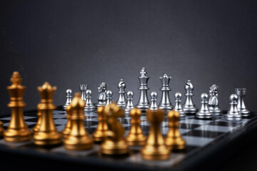 Gold and silver chess figures placed on wooden chessboard. Intellectual duel and tactical battle in...