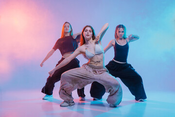 Three Young Women Performing Jazz Funk Dance in Studio with Colorful Lighting and Expressive Pose