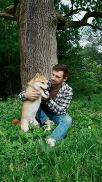young man in plaid shirt playing training petting hugging and kissing his dog during summer park walk happy loving companionship concept lifestyle	