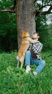 young man in plaid shirt playing training petting hugging and kissing his dog during summer park walk happy loving companionship concept lifestyle	