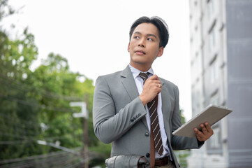 Businessman or sale agent holding tablet and thinking while looking around the land and building.