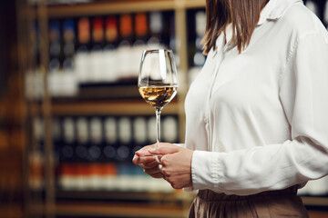 Vintner woman tasting white wine from a glass in cellar. Close up shot of female sommelier hand...