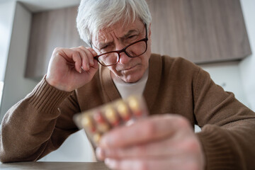 Blister pack in pensioner hand during instruction check. Age related illness, pill intake preparation, cognitive decline problems, home healthcare, visual aid assistance, pharmacy long term treatment