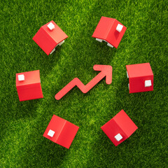 Houses on the grass and a red arrow pointing up. Rising housing prices, market growth, or increased demand for suburban living. Real estate appreciation, urban expansion, property value.