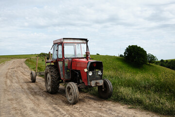 Red tractor parked on a dirt road in a hilly countryside landscape. Surrounded by green grass and...