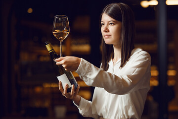 Young beautiful woman sommelier tasting white wine in the wine cellar, close up photo. Alcoholic...