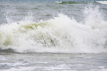 Sea waves rolling on a sandy beach. Close-up of the ocean near the coast. Background on the theme of tourism and family vacation by the water.