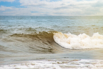 Sea waves rolling on a sandy beach. Close-up of the ocean near the coast. Background on the theme of tourism and family vacation by the water.
