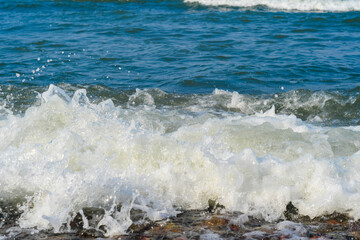 Close-up of waves crashing onto a rocky shore. Sea pebbles in the water.