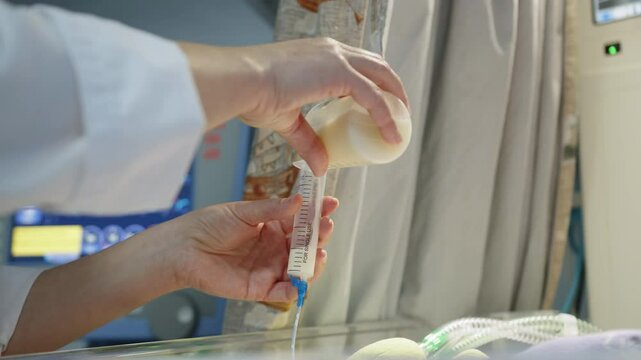 A premature baby in a neonatal intensive care unit receives nourishment from a syringe, donor breast milk. Showcasing the resource in a medical setting.