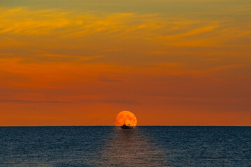 Small fishing vessel against the moon in the evening sea. Romantic landscape with a working boat at...