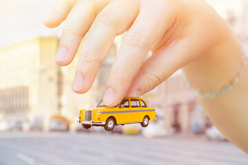 Close-up of a hand holding a toy taxi car. Background on the topic of taxi service cost and amenities.