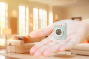 A toy washing machine on an outstretched palm. The concept of compact household appliances for a small apartment.
