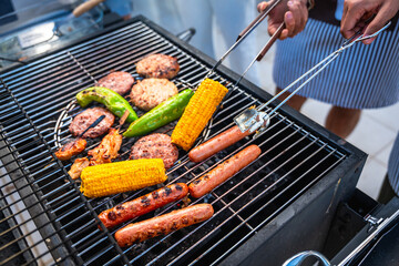 Chefs grilling hot dogs, hamburgers, corn and peppers for summer barbecue party