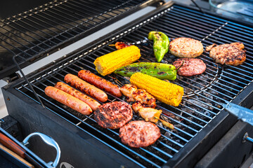 Delicious sausages, hamburgers, chicken and corn grilling on barbecue