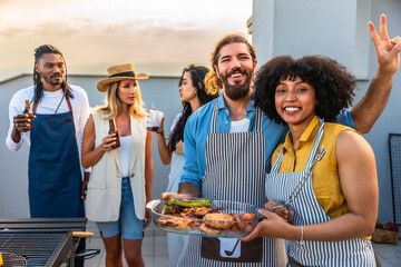 Happy chefs showing grilled food, celebrating on rooftop with friends
